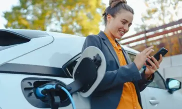 Woman leaning against hybrid car looking at her phone to claim the EV tax credit.