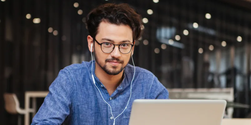 Man with earbuds in looking at a laptop