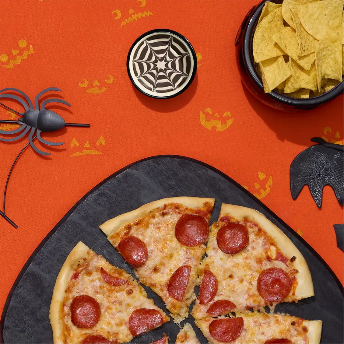 Halloween pizza party setup with pepperoni pizza, tortilla chips, and spiderweb dip
