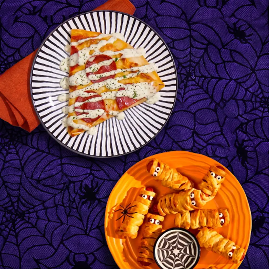 Halloween party snacks with mummy pigs in blankets, pizza, and spooky web dip