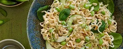 Overhead shot of ramen noodles with green onions and peas in a blue ceramic bowl.
