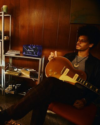 Guitarist sits in a room next to Acton III Hendrix Edition.