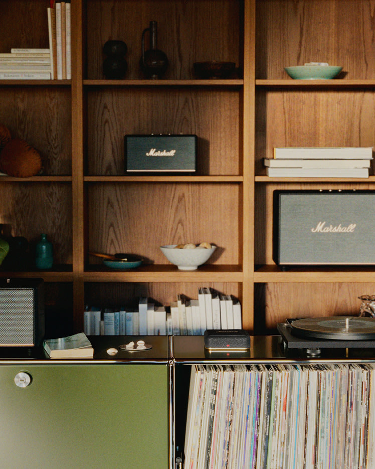 Wooden shelves with books, bowls, Marshall speakers and Heddon above a cabinet holding a record player and a large collection of vinyl records.