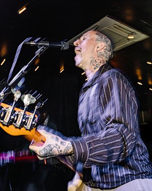 A lively person singing into a microphone while playing an electric guitar