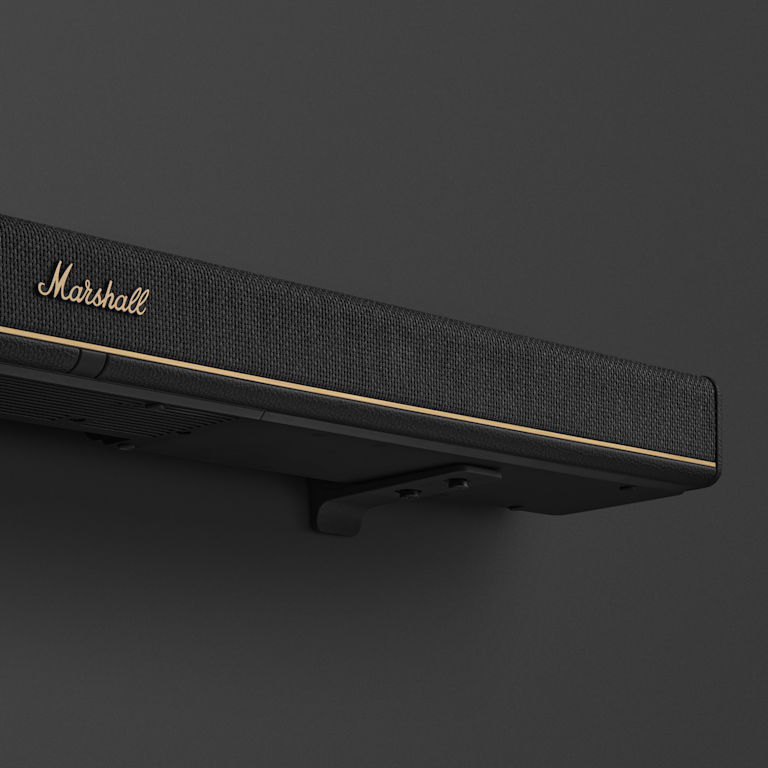 A close-up of the Marshall Heston 120 soundbar in black with gold trim, mounted on a dark wall.