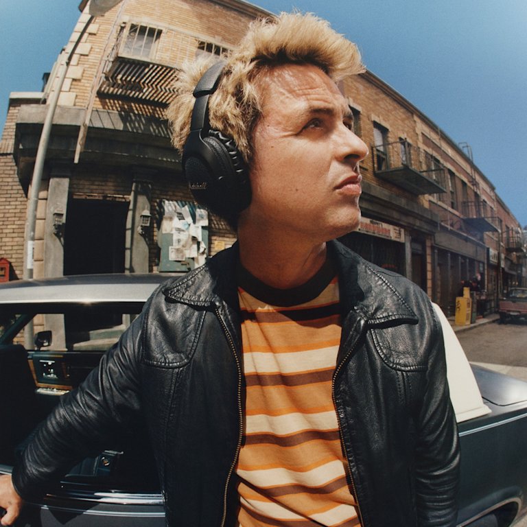 Billie Joe Armstrong wearing Marshall Monitor III A.N.C. Black over-ear headphones, stands next to a car on a street.