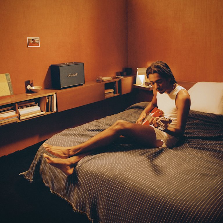 A man sitting on a bed with a Marshall WOBURN III BLACK guitar.