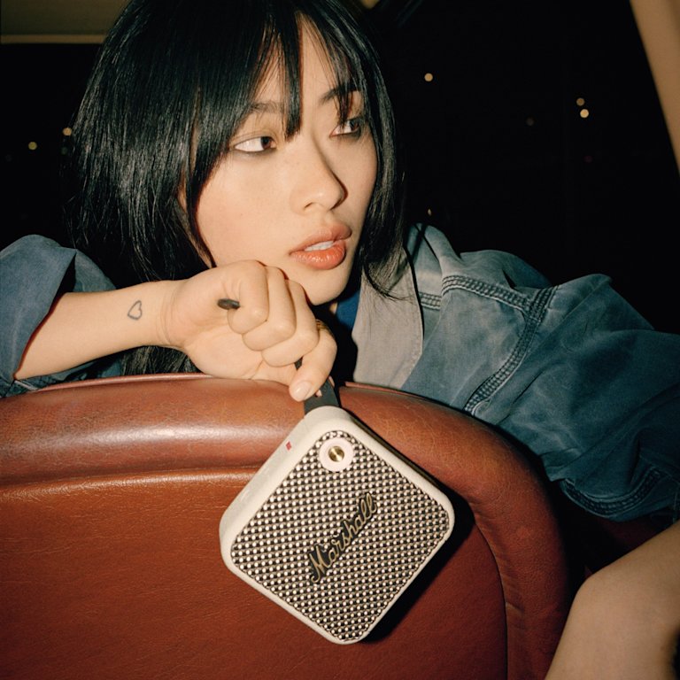 A woman sitting in the back seat of a car holding a Marshall Willen Cream speaker.