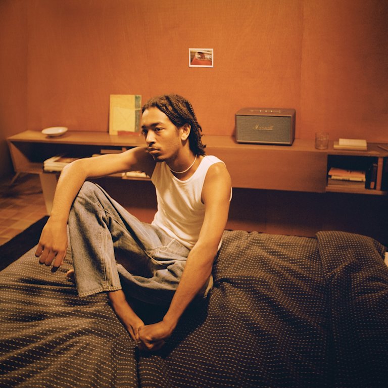 A man sitting on a bed and enjoying the powerful sound of the Marshall STANMORE III BROWN home speaker.