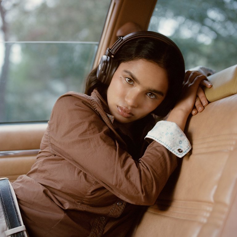 Woman with Marshall Major V Brown on-ear headphones leans against a car seat.