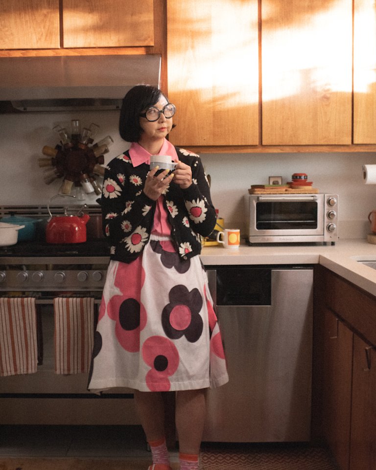 Shirley Kurata standing in a kitchen holding a cup of coffee.