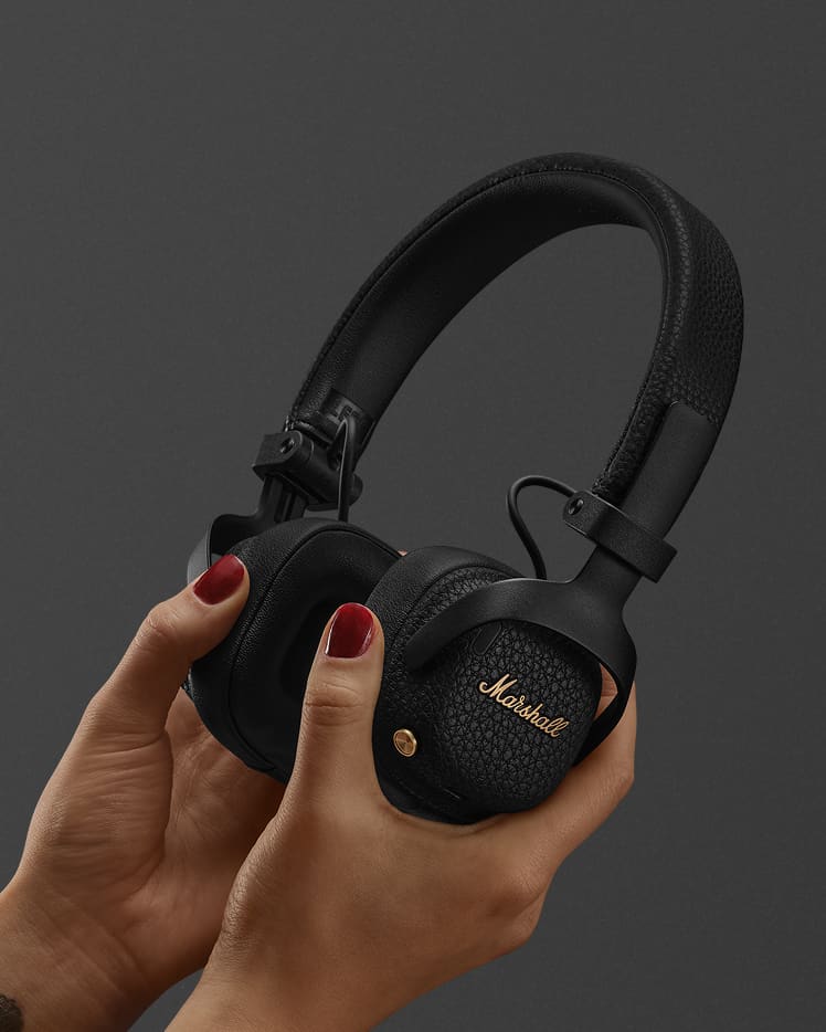 A person holds a pair of Marshall Milton A.N.C. Black headphones against a plain dark background.