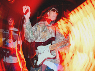 A person playing an electric guitar, surrounded by bright vibrant colors