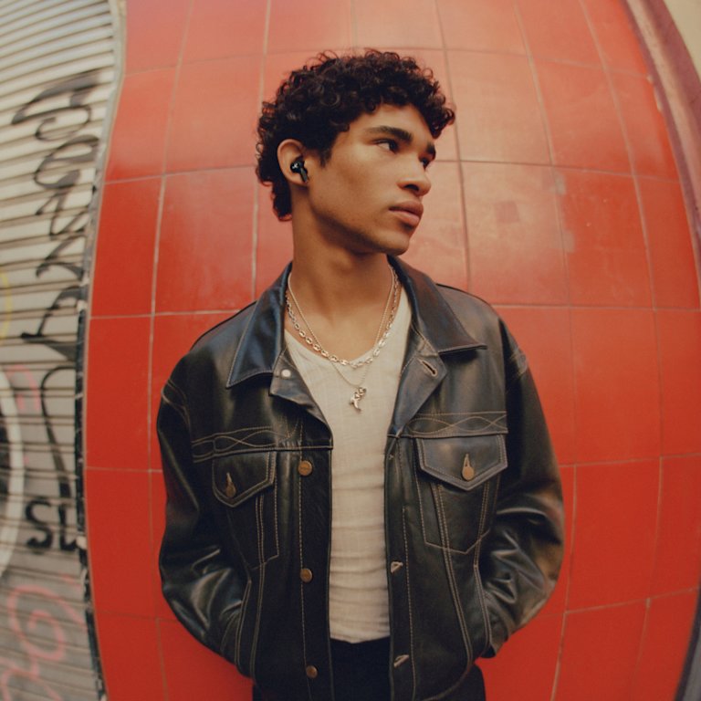 A young man in a Marshall leather jacket standing in front of a red wall.