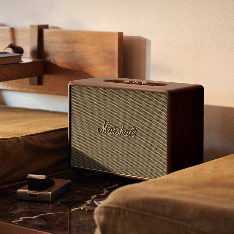 Marshall Woburn III Brown speaker sits on a wooden table, surrounded by brown cushions in a cozy room.