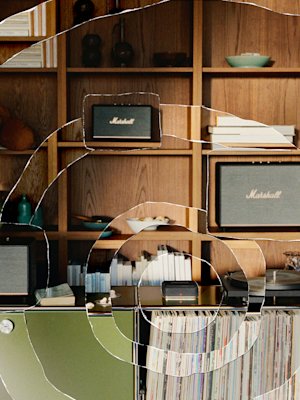 A wooden shelf holds books, bowls, and three Marshall speakers. Below, a green cabinet displays Heddon and a record player.