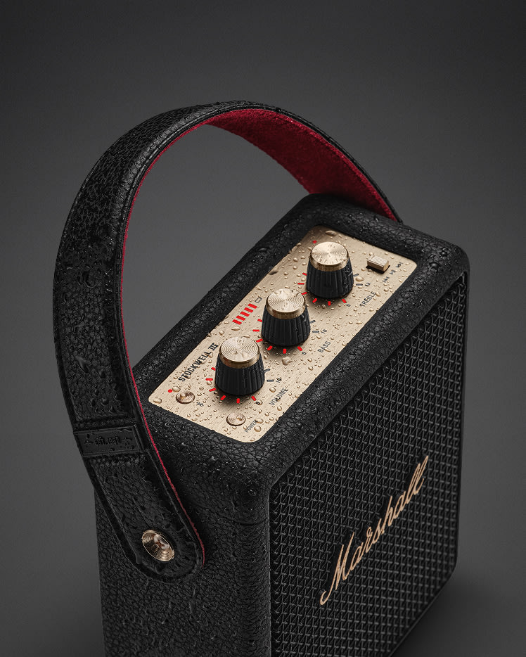 Stockwell III Black and Brass portable speaker shown with water droplets on its surface.