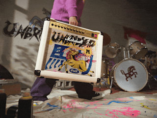 A person holds a Studio 900 Combo Lunar New Year Edition 2026; drums and paint-covered floor are in the background.