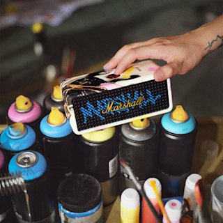 A hand places Emberton III Lunar New Year Edition 2026 speaker on top of a group of colorful spray paint cans arranged on a table.