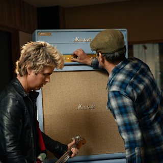 An image of Billie Joe Armstrong who holds a guitar while another person is adjusting the controls on the blue Marshall 1959BJA amplifier.