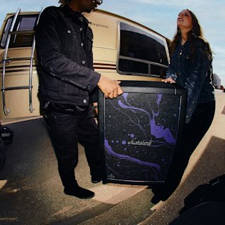 Two people stand by an RV, holding a JMH 212 Cab with a purple and black design on its front.