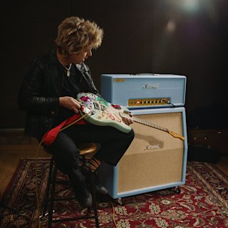 Billie Joe Armstrong sits on a stool playing an electric guitar in front of a Marshall 1959 BJA Artist Signature amplifier stack.