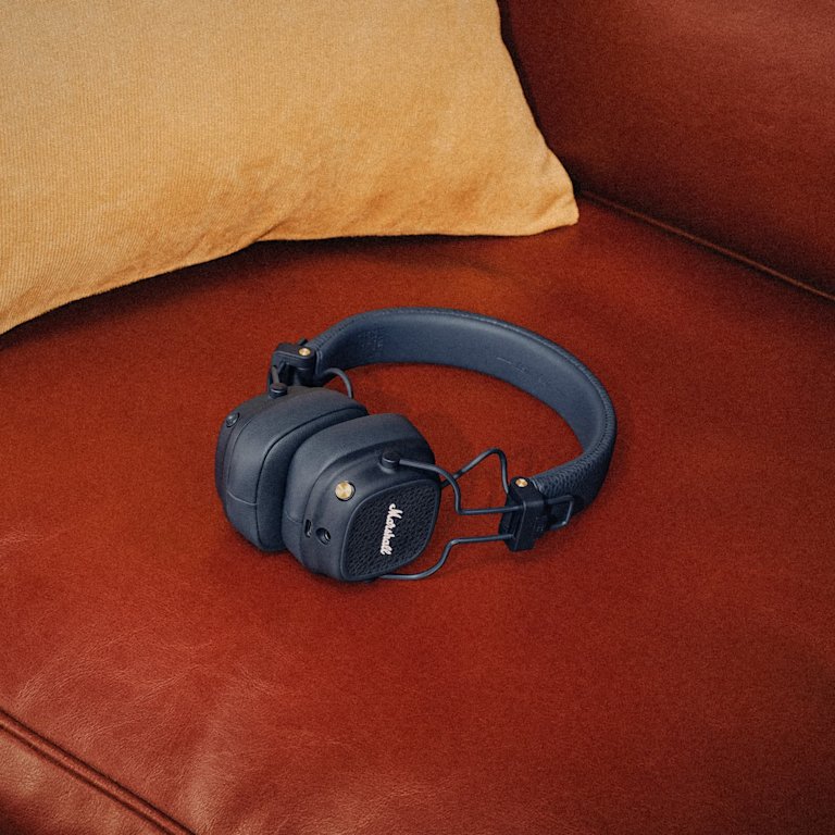 Major V Midnight Blue Bluetooth headphones rest on a brown leather couch beside a tan pillow.