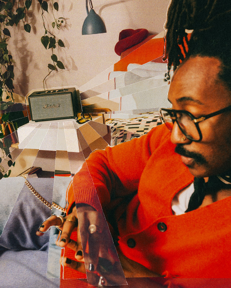 A person wearing glasses and an orange sweater sits on a couch toward a Marshall Acton IV Black speaker on a table in a cozy, plant-filled room.