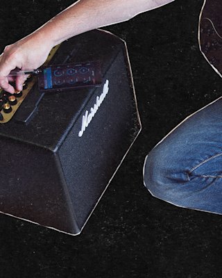 Someone adjusts the knobs on a Marshall MG10 combo amplifier while holding an electric guitar.