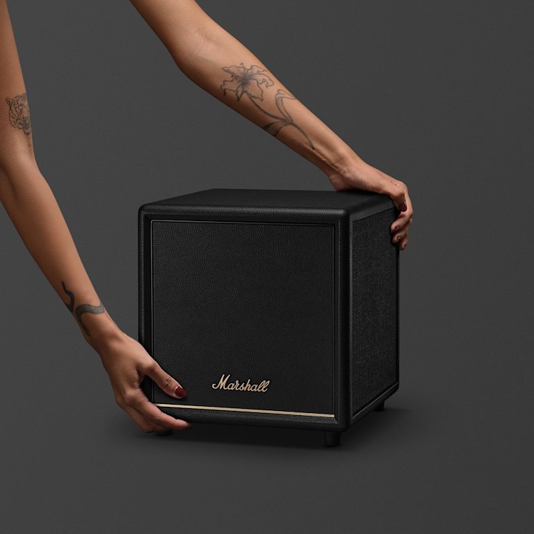 A tattooed individual places a Marshall Heston Sub 200 Black on a dark surface.