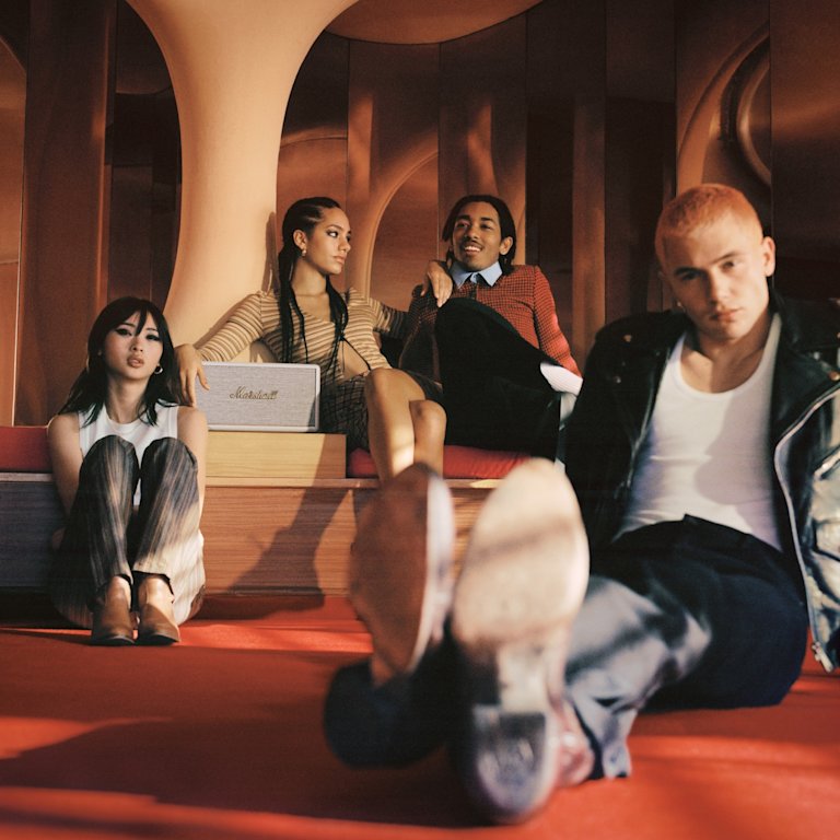 A group of people sitting on the floor, surrounded by a white Marshall Stanmore III speaker.