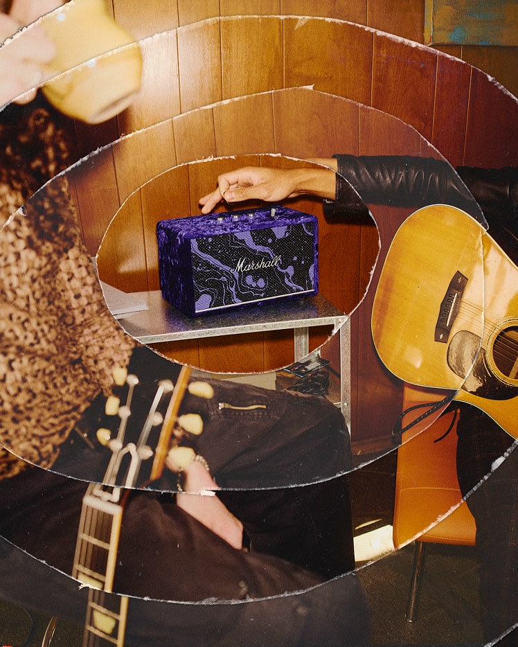Two people next to a small table with a Acton III Marshall x Hendrix 60th Anniversary Edition speaker; one person holds a mug, and another adjusts the speaker.