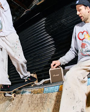 Two people on a skate ramp with a portable Marshall Stockwell III Cream speaker placed between them. One is skateboarding while the other is seated.