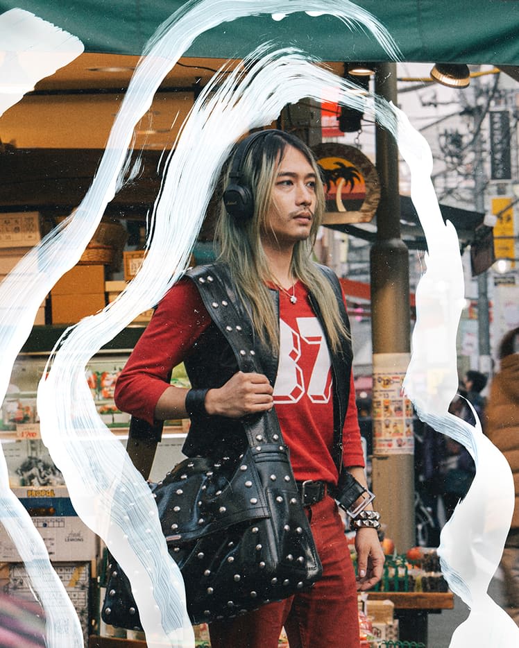 A person with wearing Milton A.N.C. Black headphones, a red outfit, and a studded black bag stands on a busy street with market stalls.