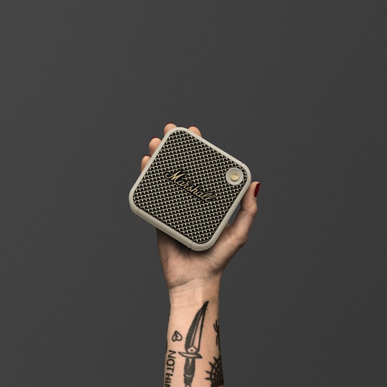 A tattooed hand holding a Marshall Willen Cream portable speaker. Easy to carry around, the Marshall Willen it a small and practical speaker.