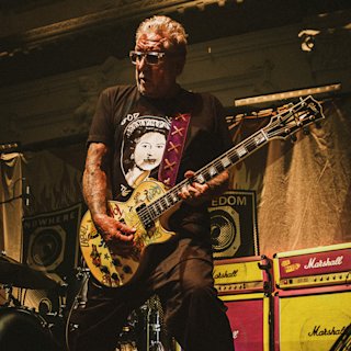 Steve Jones from Sex Pistols plays an electric guitar covered in stickers on stage.