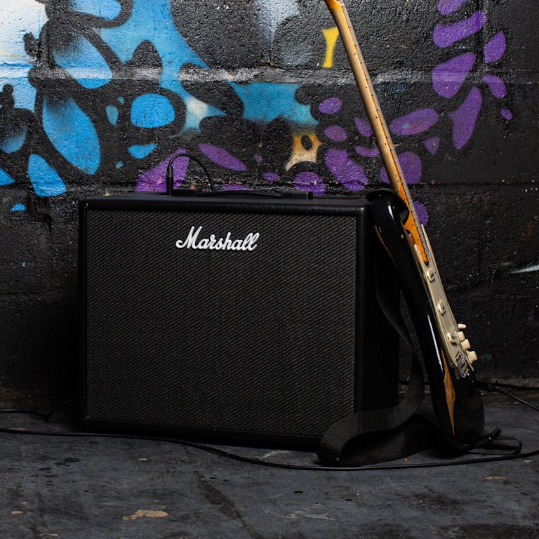 Front view of the Marshall CODE50 Combo and guitar in front of graffiti wall.