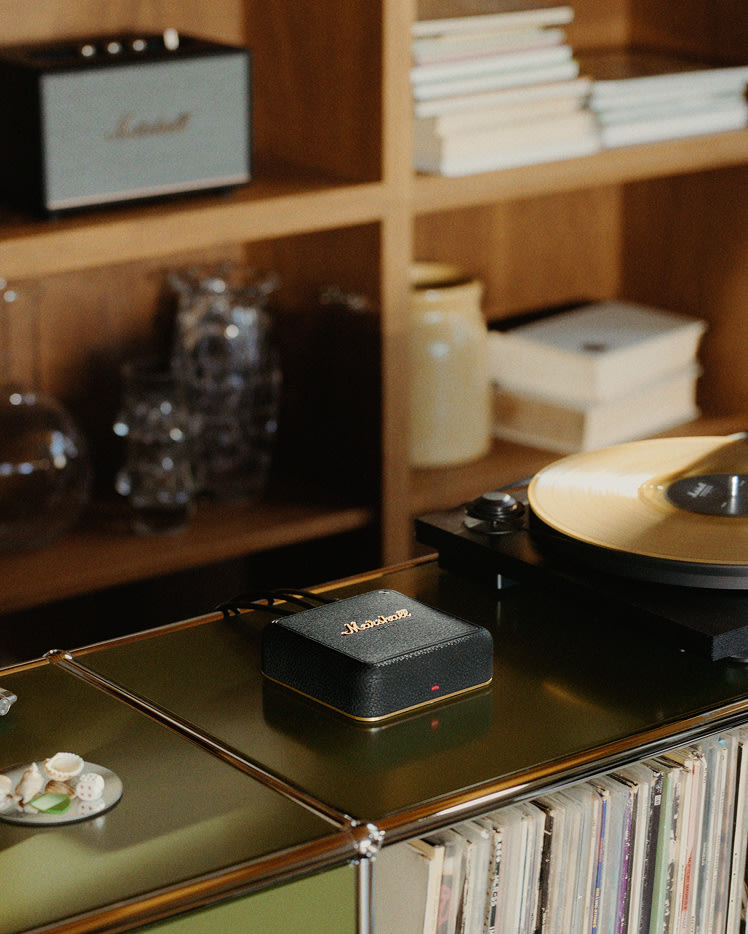 A record player with a yellow vinyl sits on a shelf next to Marshall Heddon, with books and glassware in the background.