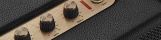 A hand plugs a USB-C power cord into the back panel of a Kilburn III portable speaker.