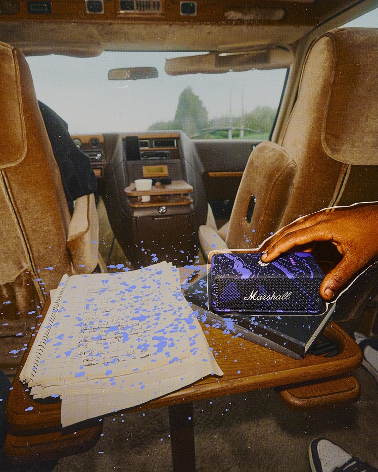 Emberton III Hendrix Edition speaker on a fold-out table in a car, next to a notebook.