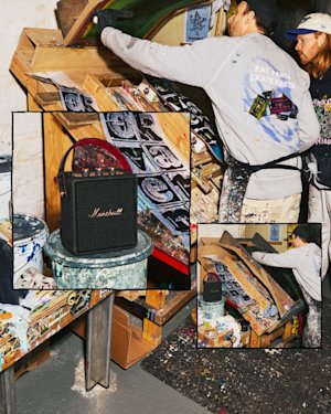 A person customizing his skateboard deck at an art studio table covered in prints and supplies; a Marshall Stockwell III speaker sits nearby.