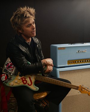 Billie Joe Armstrong sits on a stool holding an electric guitar with stickers and "BJ" letters, next to a Marshall 1959 BJA Artist Signature.