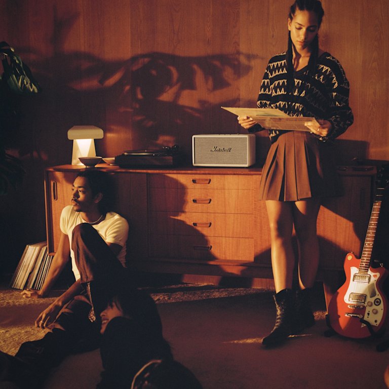 A group of people enjoying the immersive sound of a Stanmore III Cream home speaker by Marshall as they lay on the floor in front of it.