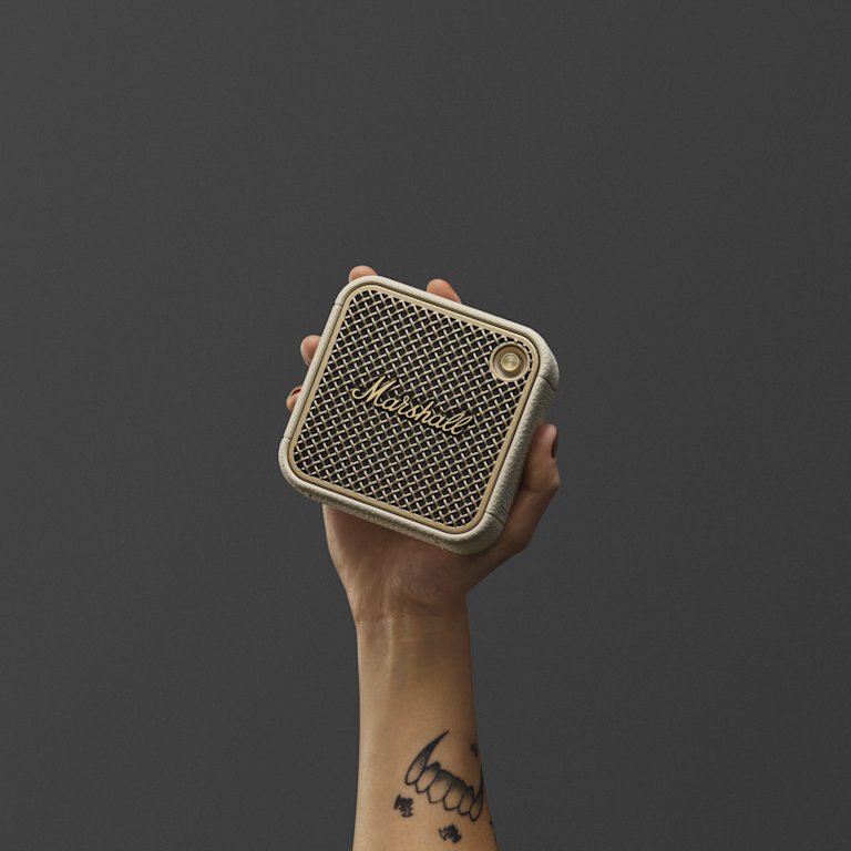 A person holding a Marshall Willen II Cream bluetooth speaker with a mesh front.