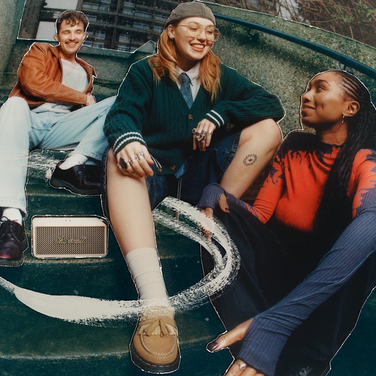 Three people sit on outdoor steps, while music plays from the Marshall Middleton II Cream portable Bluetooth speaker nearby.