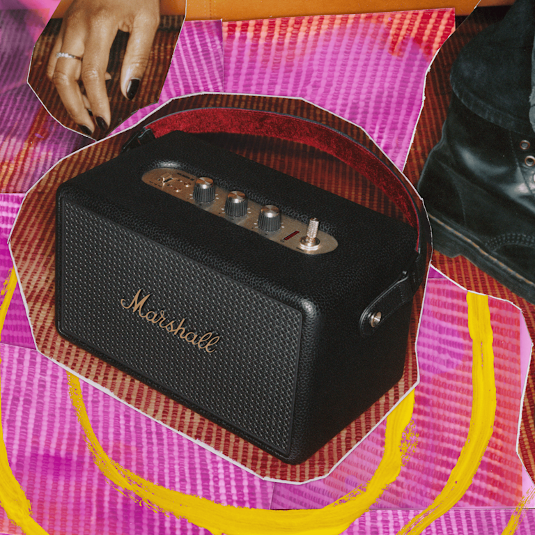 Marshall Kilburn III Black and Brass portable speaker on a textured pink and yellow surface.