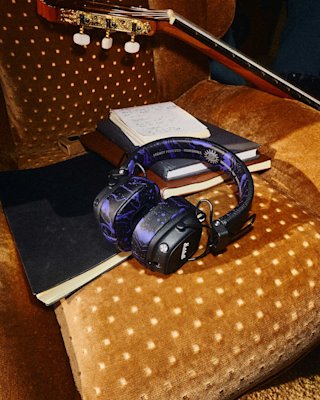 Major V Hendrix Edition headphones rests on notebooks on a brown dotted chair, with a guitar nearby.