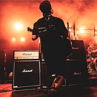 A person is playing a guitar live on stage with a orange tint