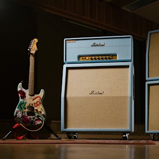 Billie Joe Armstrong's Eectric guitar with BJ stickers leans against a Marshall 1959BJA amplifier in a dimly lit room.
