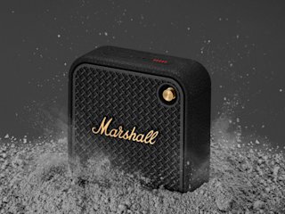 Enceinte bluetooth Marshall Willen II noir et laiton posée sur une surface poussiéreuse.